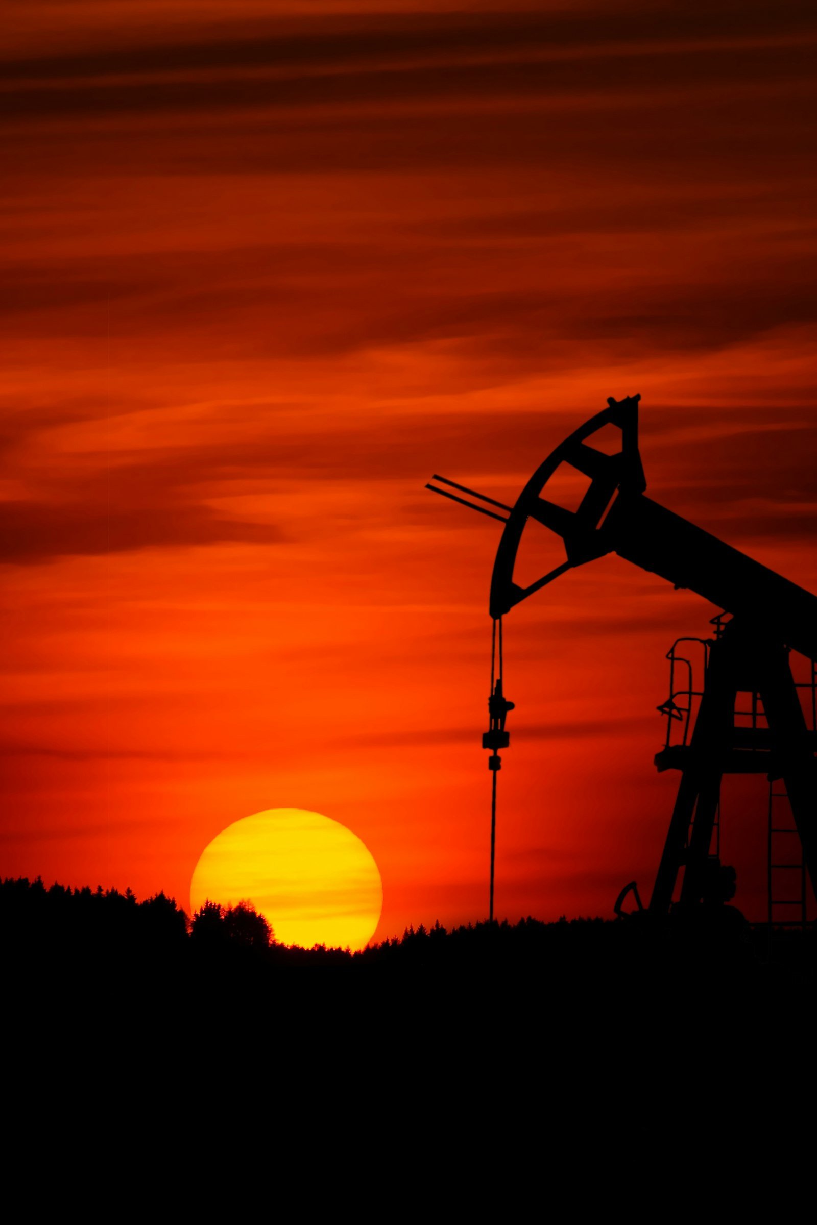 An oil pump jack silhouetted against a vivid sunset, representing global energy infrastructure.