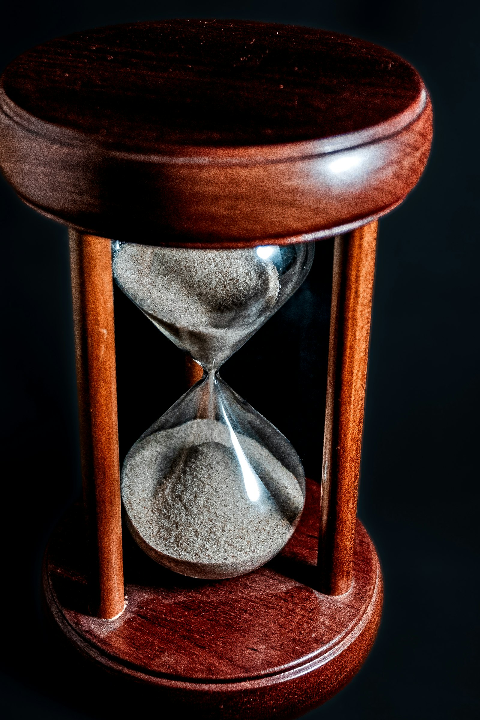 Close-up of a wooden hourglass with sand flowing through it against a dark background, representing the fixed term and predictable timeline of a fixed deposit investment.